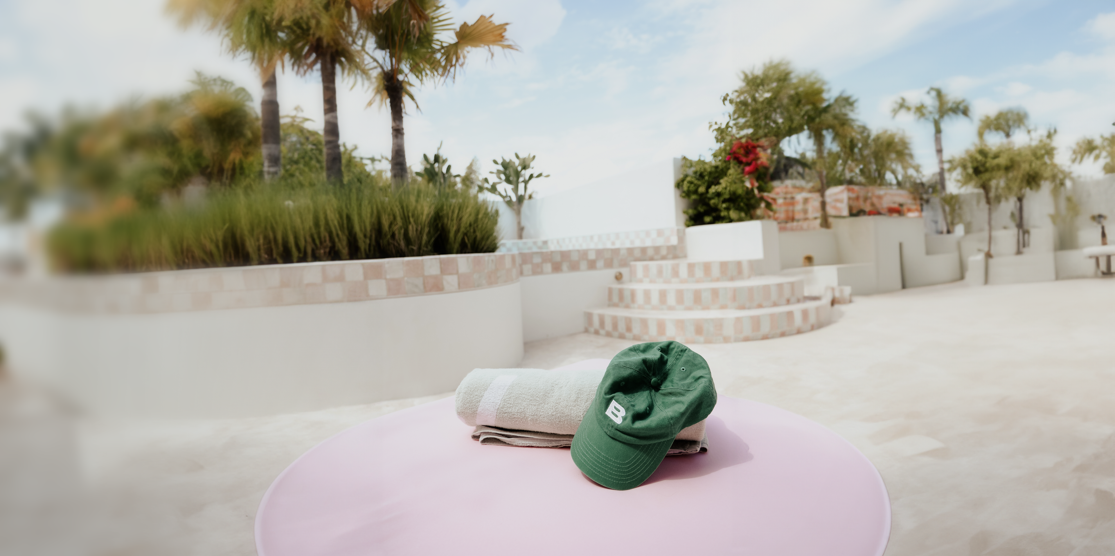 Poolside scene featuring Byron Sun merchandise, including a hat and towel, epitomizing luxury and relaxation in a sunlit setting