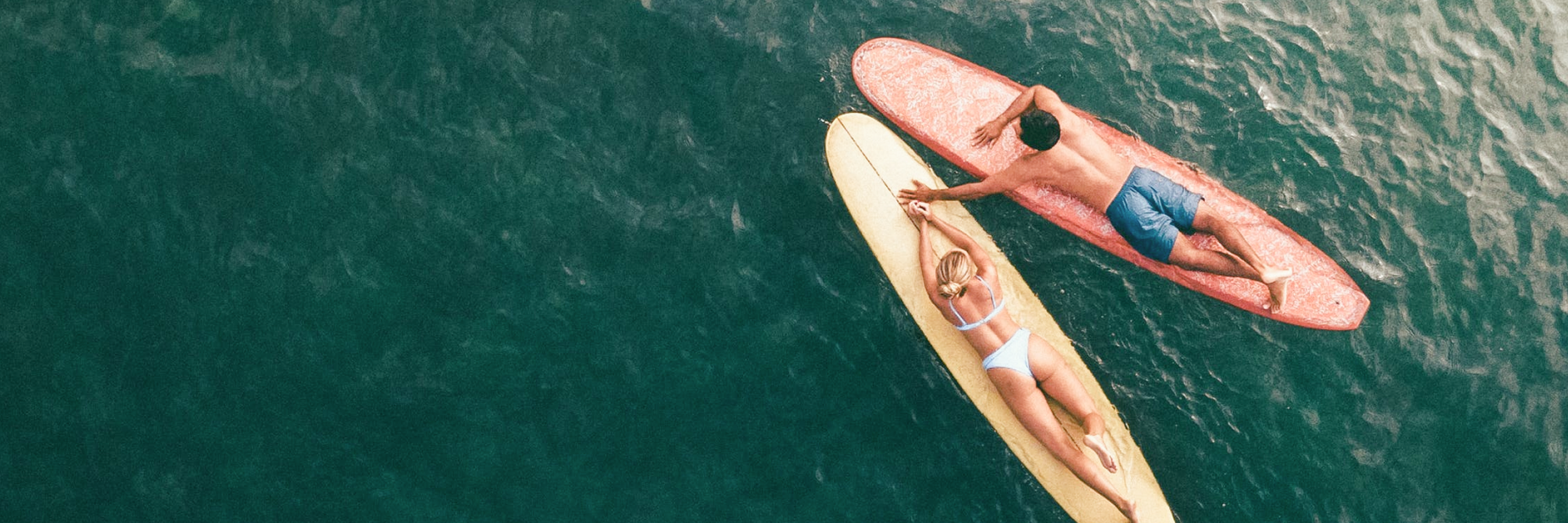 Aerial view of a man and a woman holding hands while riding longboards, reflecting the carefree and adventurous spirit embodied by Byron Sun's ethos